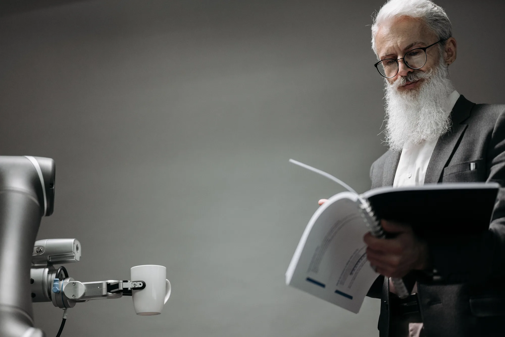 A man reading a document beside a robotic arm on a workbench